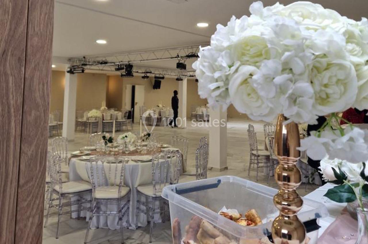Salle de réception décorée avec des tables rondes, des chaises transparentes et des fleurs blanches sur les tables.