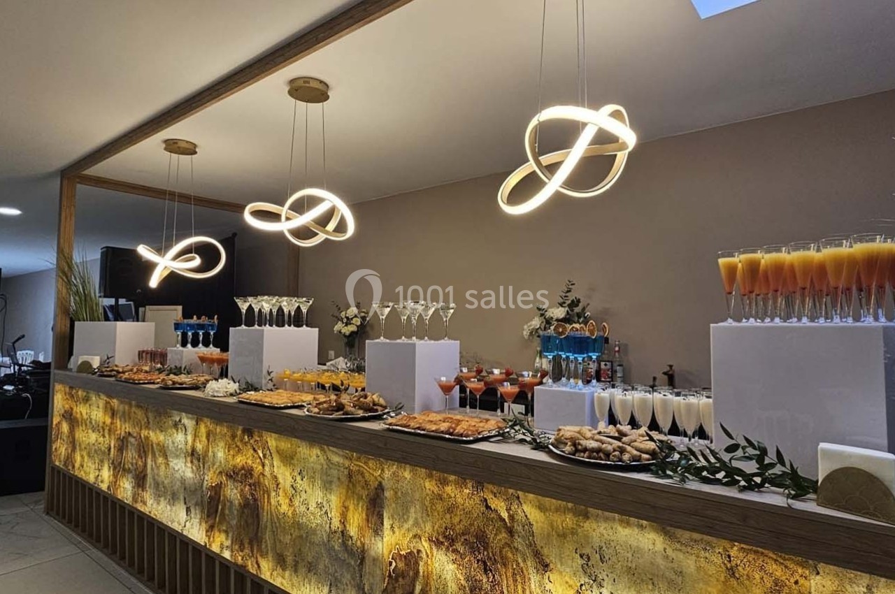 Buffet élégant avec verrines, cocktails et amuse-bouches, présenté sous des luminaires modernes dans une salle de réception.