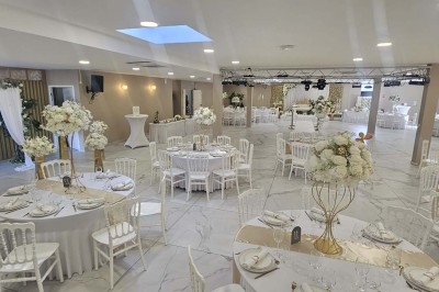 Salle de réception décorée avec des fleurs blanches, un canapé élégant sur une estrade et des tables dressées.