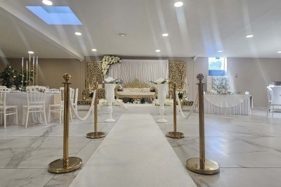 Salle de réception décorée avec des fleurs blanches, un canapé élégant sur une estrade et des tables dressées.