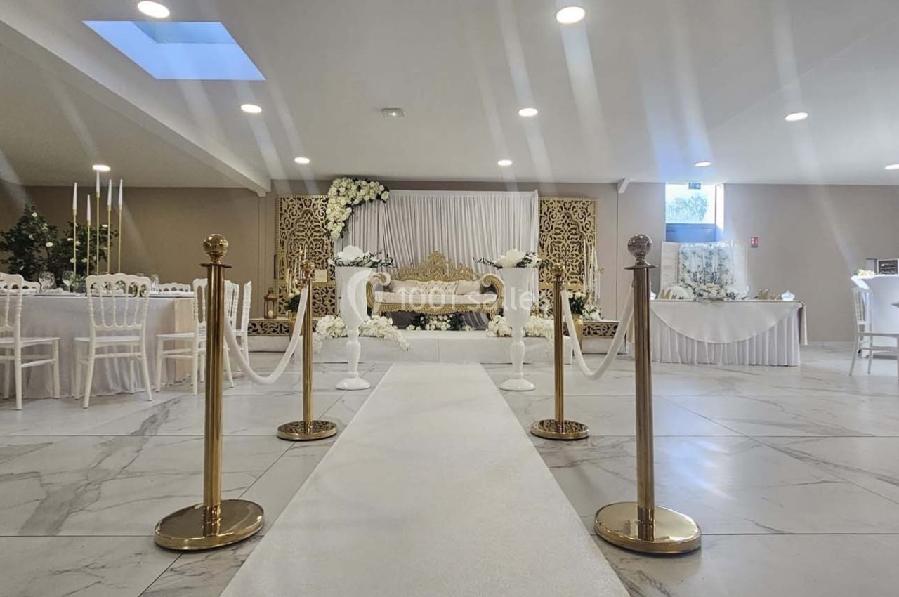 Salle de réception décorée en blanc et or, avec une allée centrale menant à une estrade ornée de fleurs.