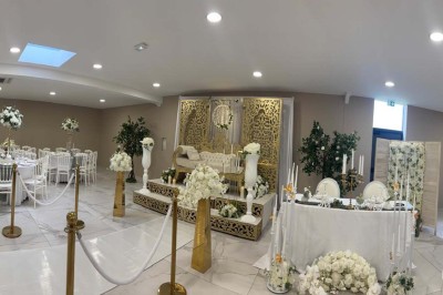 Salle de réception décorée avec des fleurs blanches, un canapé élégant sur une estrade et des tables dressées.