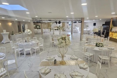 Salle de réception décorée avec des fleurs blanches, un canapé élégant sur une estrade et des tables dressées.