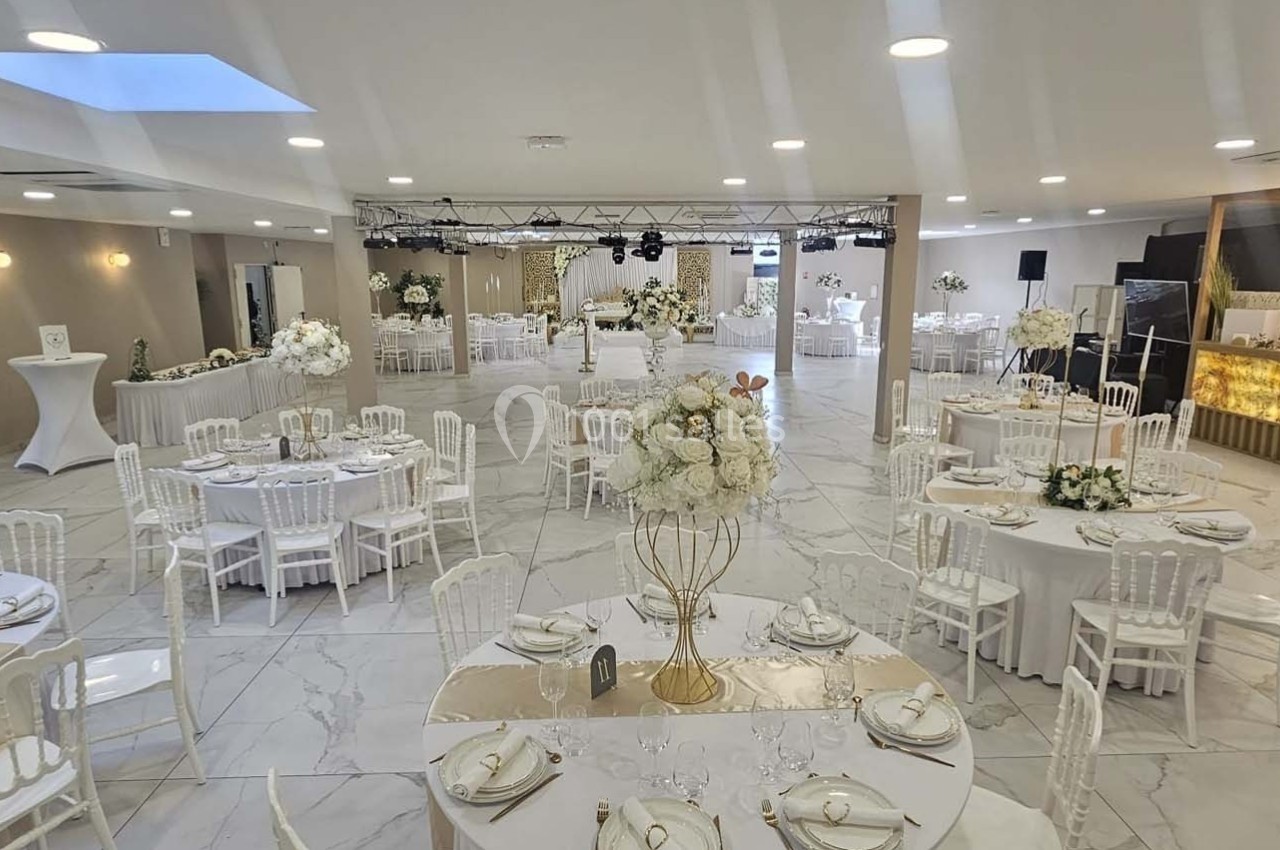 Salle de réception élégante avec tables rondes décorées de fleurs blanches et espace lumineux au sol en marbre.