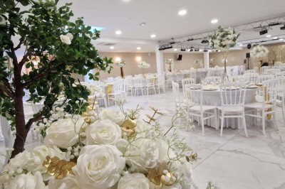 Salle de réception décorée avec des fleurs blanches, un canapé élégant sur une estrade et des tables dressées.