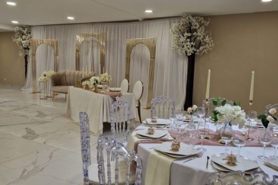 Salle de réception décorée avec des fleurs blanches, un canapé élégant sur une estrade et des tables dressées.