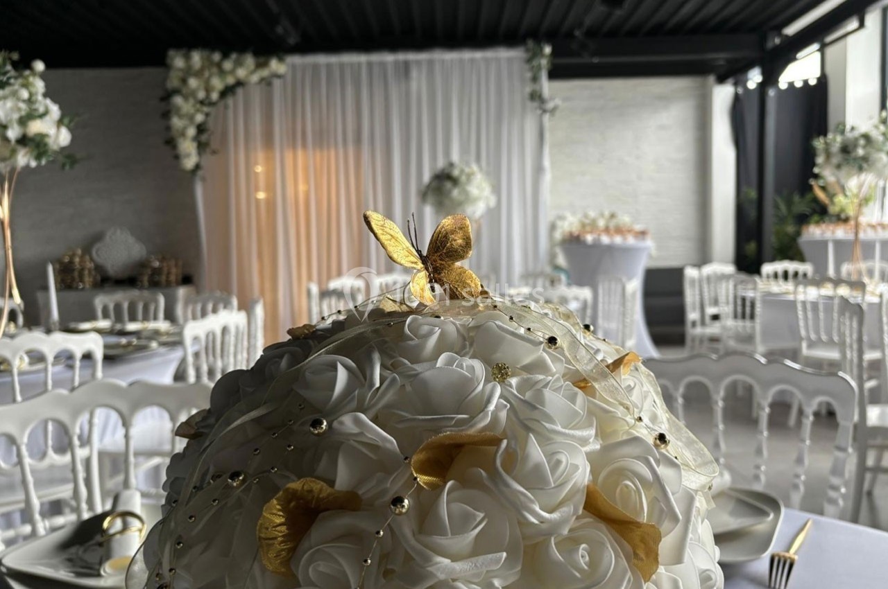 Centre de table en roses blanches artificielles avec décorations dorées, dans une salle de réception élégante.