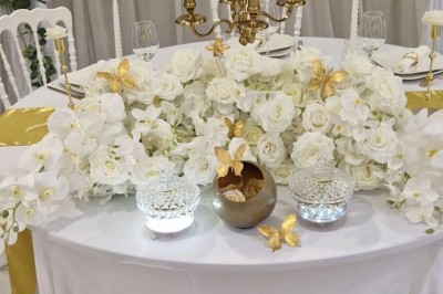 Salle de réception décorée avec des fleurs blanches, un canapé élégant sur une estrade et des tables dressées.