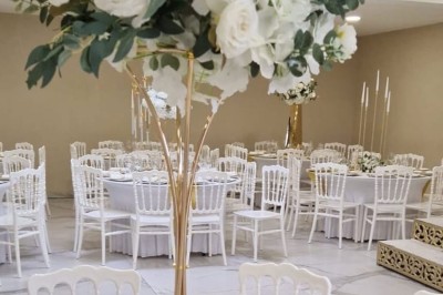 Salle de réception décorée avec des fleurs blanches, un canapé élégant sur une estrade et des tables dressées.