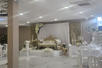 Salle de réception décorée avec des fleurs blanches, un canapé élégant sur une estrade et des tables dressées.