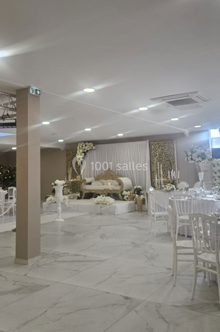 Salle de réception décorée avec des fleurs blanches, un canapé élégant sur une estrade et des tables dressées.
