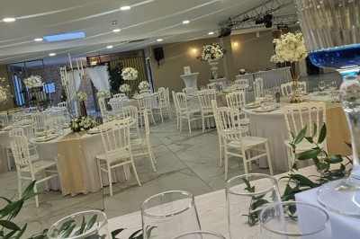 Salle de réception décorée avec des fleurs blanches, un canapé élégant sur une estrade et des tables dressées.