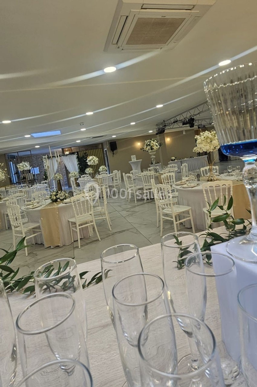 Salle de réception élégamment décorée avec des tables rondes, des chaises blanches et des arrangements floraux.