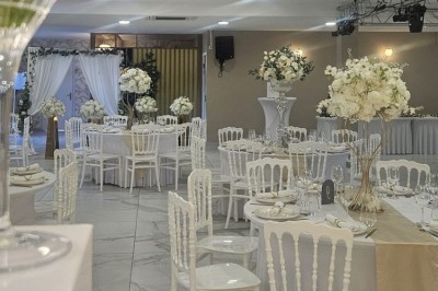 Salle de réception décorée avec des fleurs blanches, un canapé élégant sur une estrade et des tables dressées.