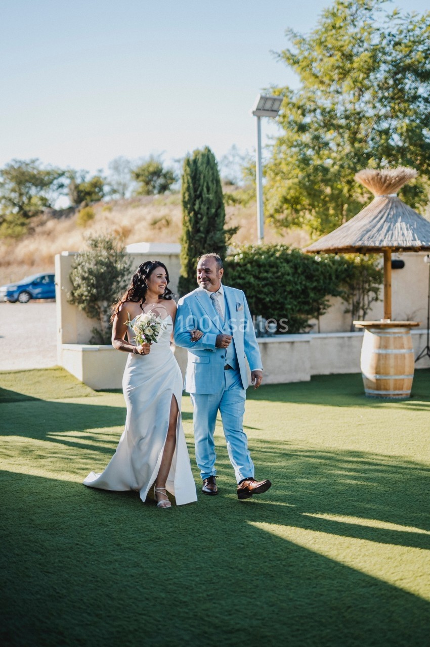 Une femme en robe blanche et un homme en costume bleu marchent côte à côte sur une pelouse par une journée ensoleillée.