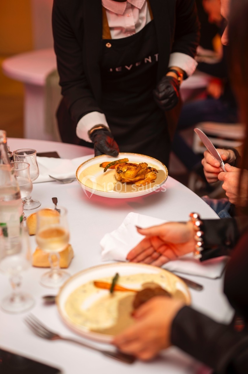 Un serveur dépose une assiette contenant un plat préparé sur une table dressée pour un repas.