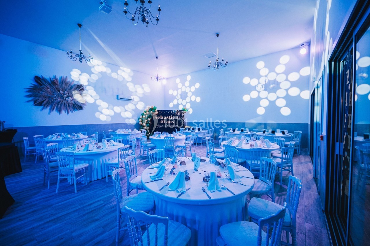 Salle de réception décorée avec des tables rondes dressées, éclairage bleu et motifs lumineux sur les murs.