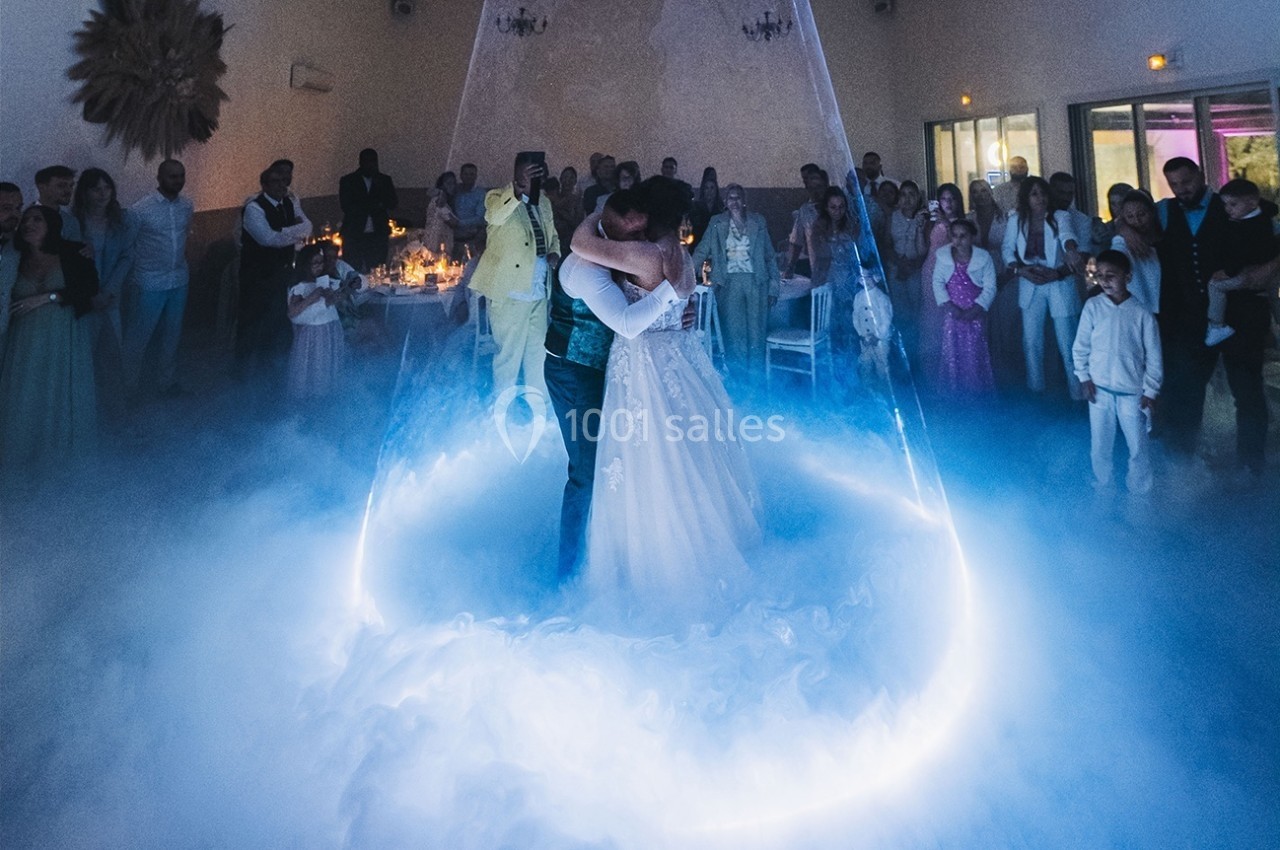 Un couple danse au centre d'une piste entourée de fumée et de lumière, sous le regard des invités.