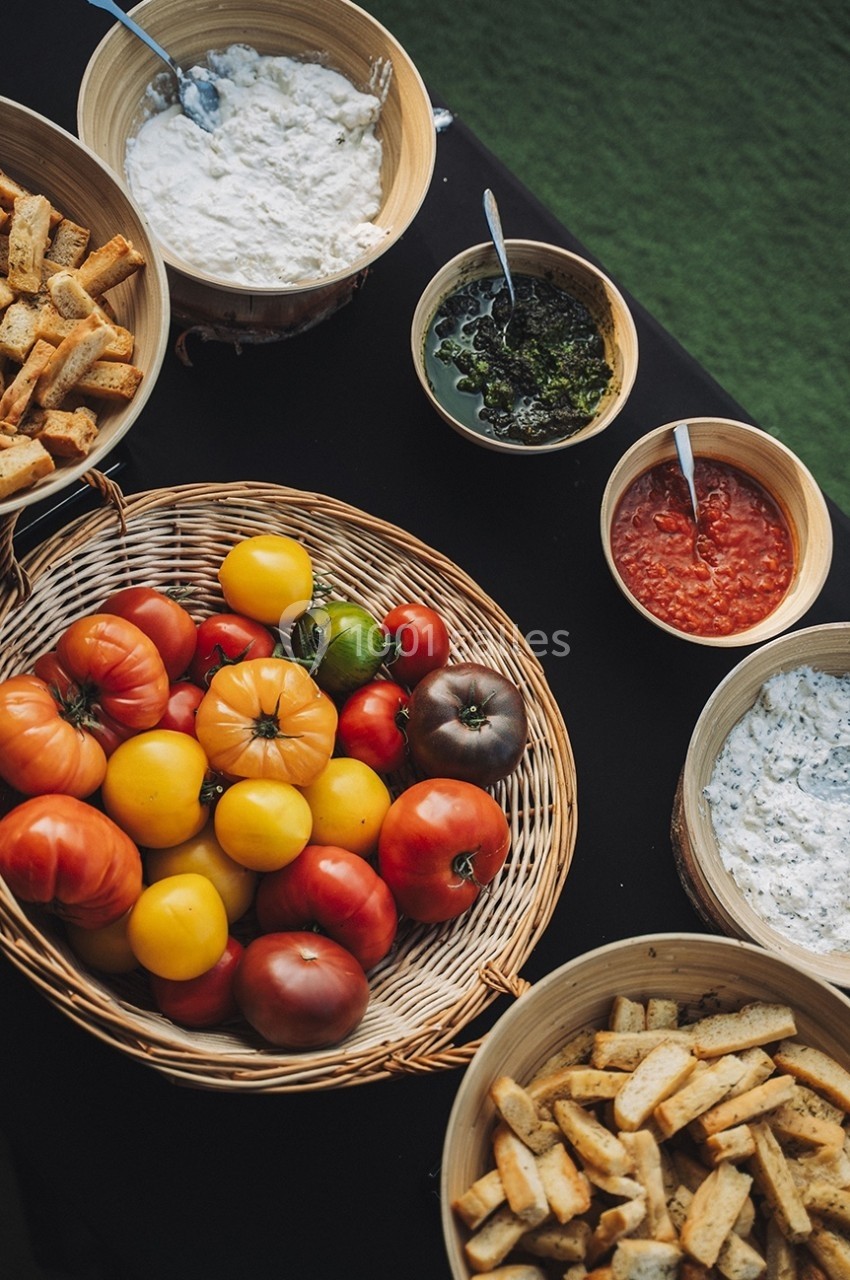 Assortiment de tomates colorées, pains grillés et sauces variées présentés dans des bols sur une table noire.