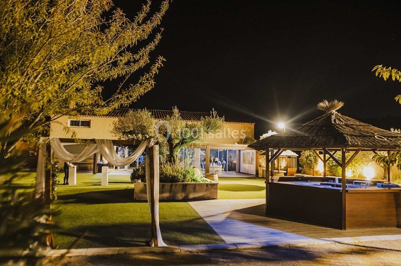 Vue nocturne d'un espace extérieur aménagé avec une pergola, un jacuzzi et un jardin éclairé.