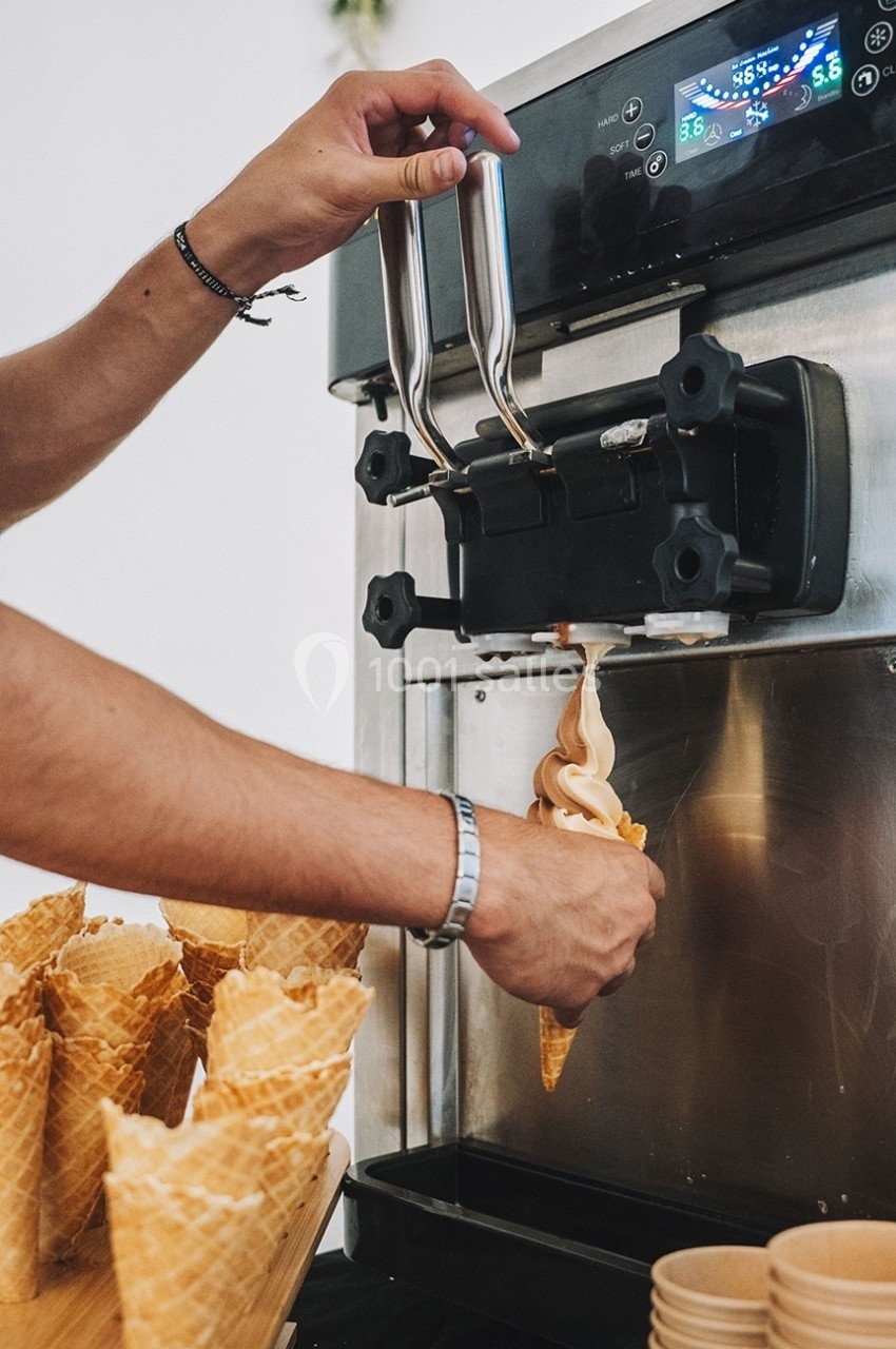 Une personne sert une glace à l'italienne dans un cornet à l'aide d'une machine à glace automatique.