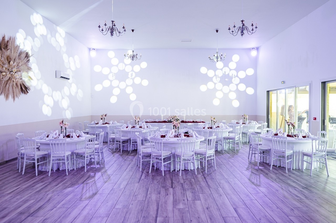 Salle de réception décorée avec des tables rondes, chaises blanches et éclairage lumineux projetant des motifs au mur.