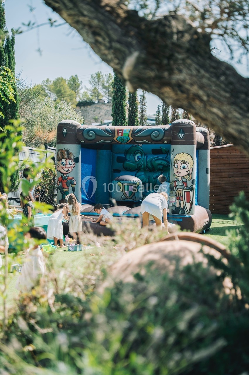 Enfants jouant autour et à l'intérieur d'un château gonflable décoré de personnages médiévaux dans un jardin.
