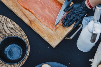 Une personne tranche un filet de saumon sur une planche en bois, avec des toasts préparés en premier plan.
