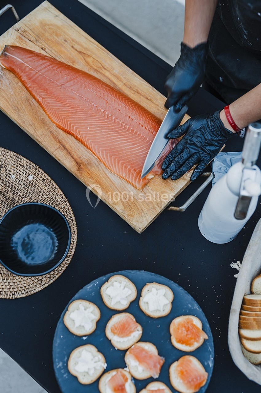Une personne tranche un filet de saumon sur une planche en bois, avec des toasts préparés en premier plan.