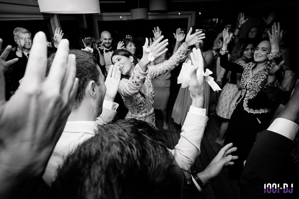 Groupe de personnes dansant et levant les bras lors d'une fête dans une ambiance animée en noir et blanc.