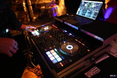 Table de mixage DJ sur une plage au coucher du soleil, avec des tables dressées en arrière-plan près de la mer.