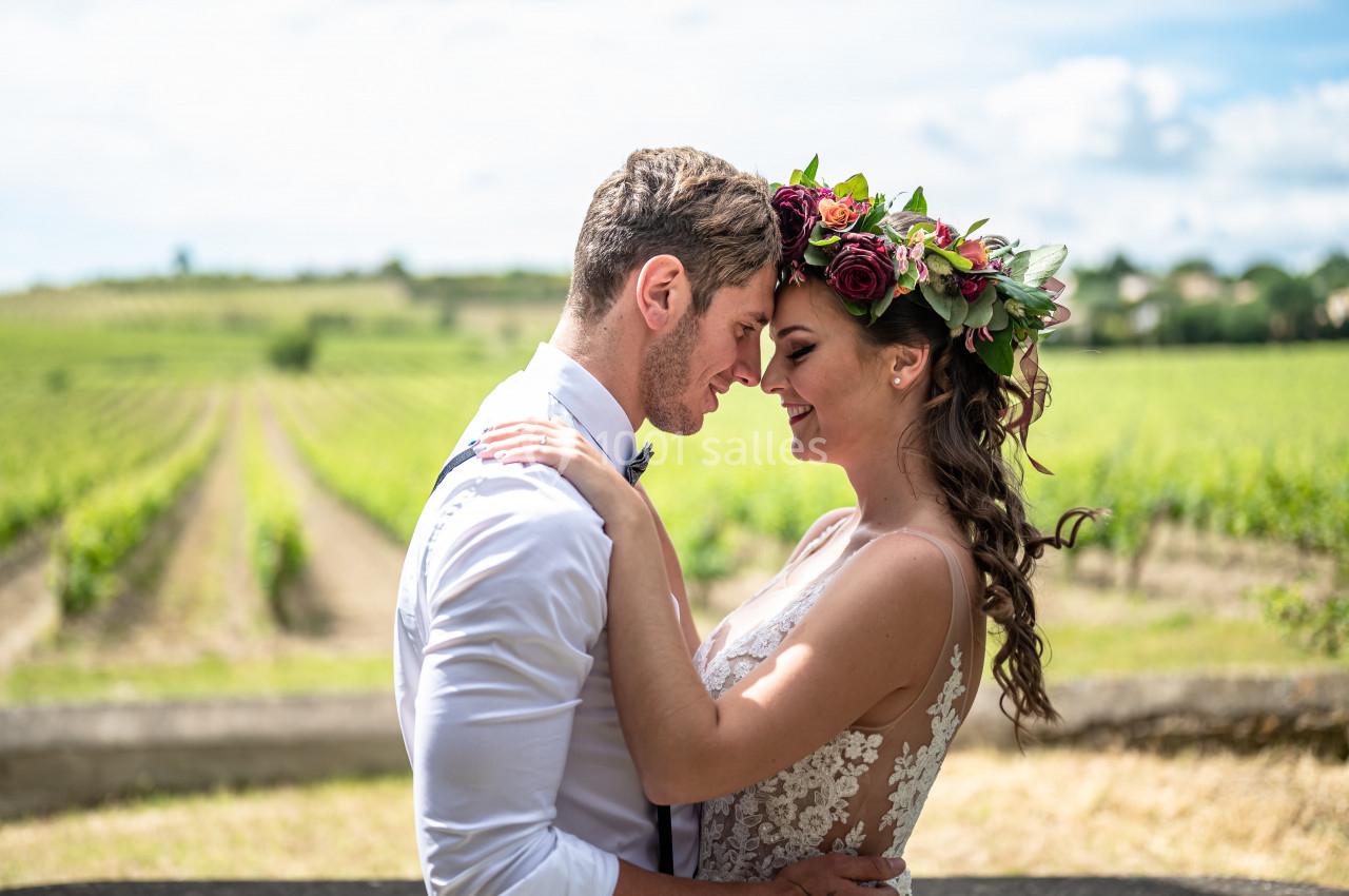 Un couple en tenue de mariage s'enlace dans un vignoble sous un ciel ensoleillé.