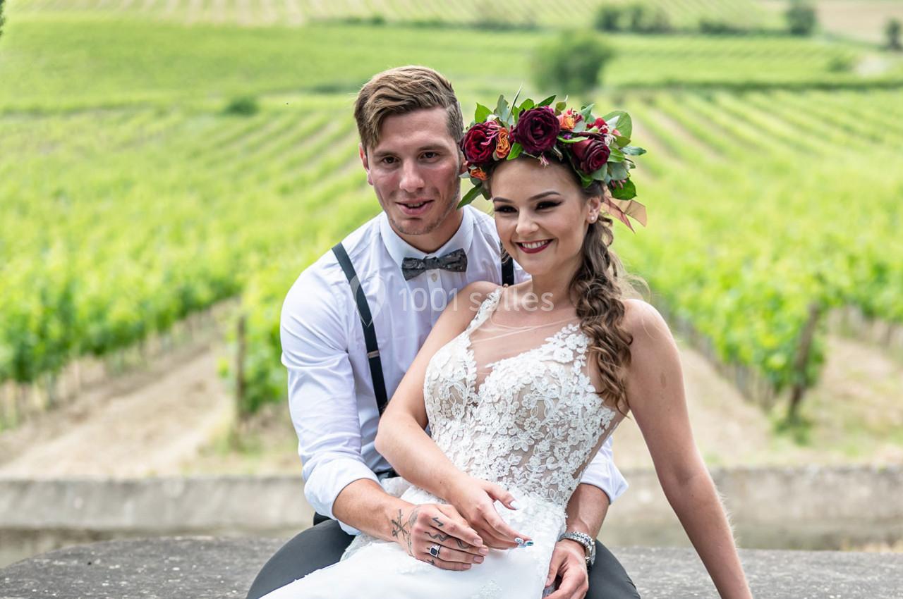 Un couple de mariés sourit devant un paysage de vignobles verdoyants.
