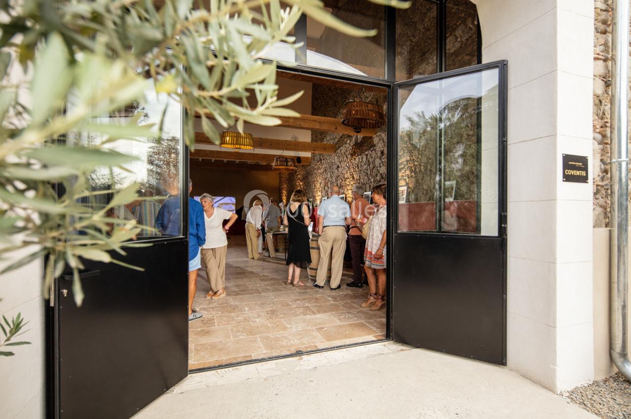 Entrée ouverte d'un bâtiment en pierre, avec des personnes rassemblées à l'intérieur dans un espace lumineux.
