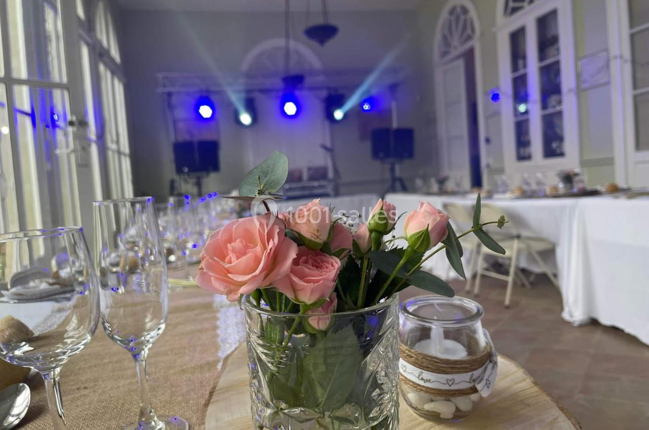 Vase de roses roses sur une table décorée, avec une salle lumineuse et une scène éclairée en arrière-plan.