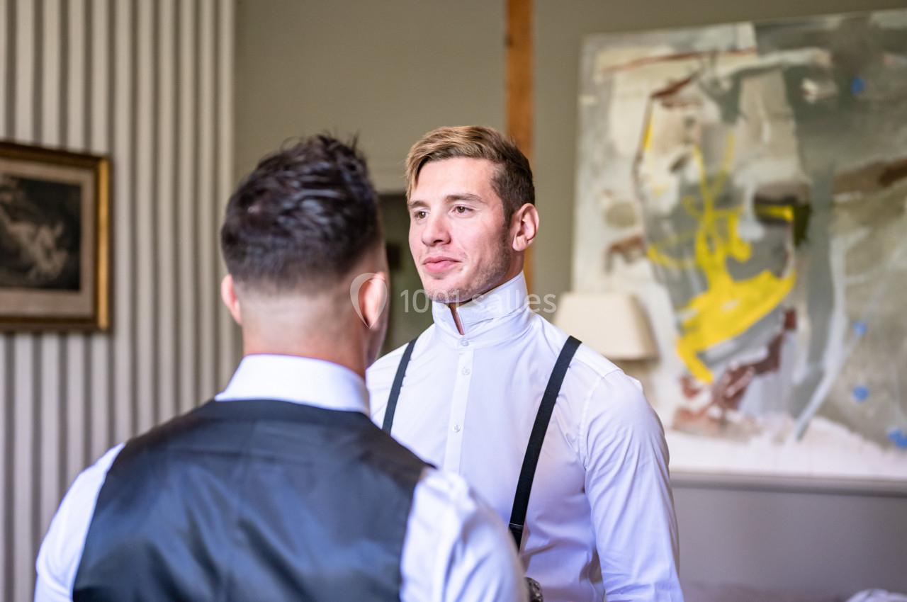 Deux hommes en tenue formelle discutent dans une pièce décorée avec un tableau abstrait et des murs clairs.