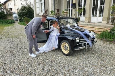 Un marié aide sa partenaire en robe de mariée à sortir d'une voiture ancienne décorée pour un mariage.