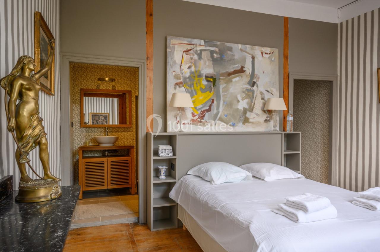 Chambre lumineuse avec lit double, décoration artistique, statue dorée et vue sur une salle de bain attenante.