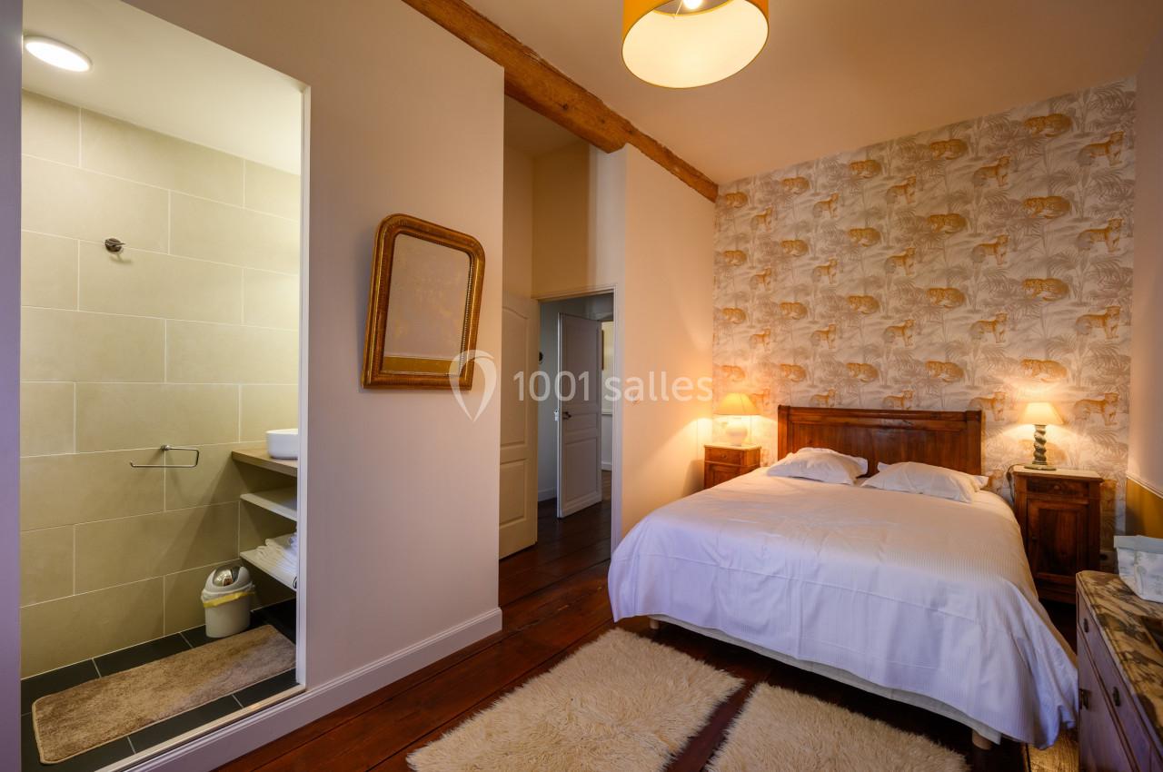 Chambre avec lit double, murs décorés, tapis au sol, et salle de bain attenante avec douche visible.