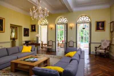 Salle en pierre avec de grandes tables dressées, éclairée par des lustres faits de bouteilles en verre vert.