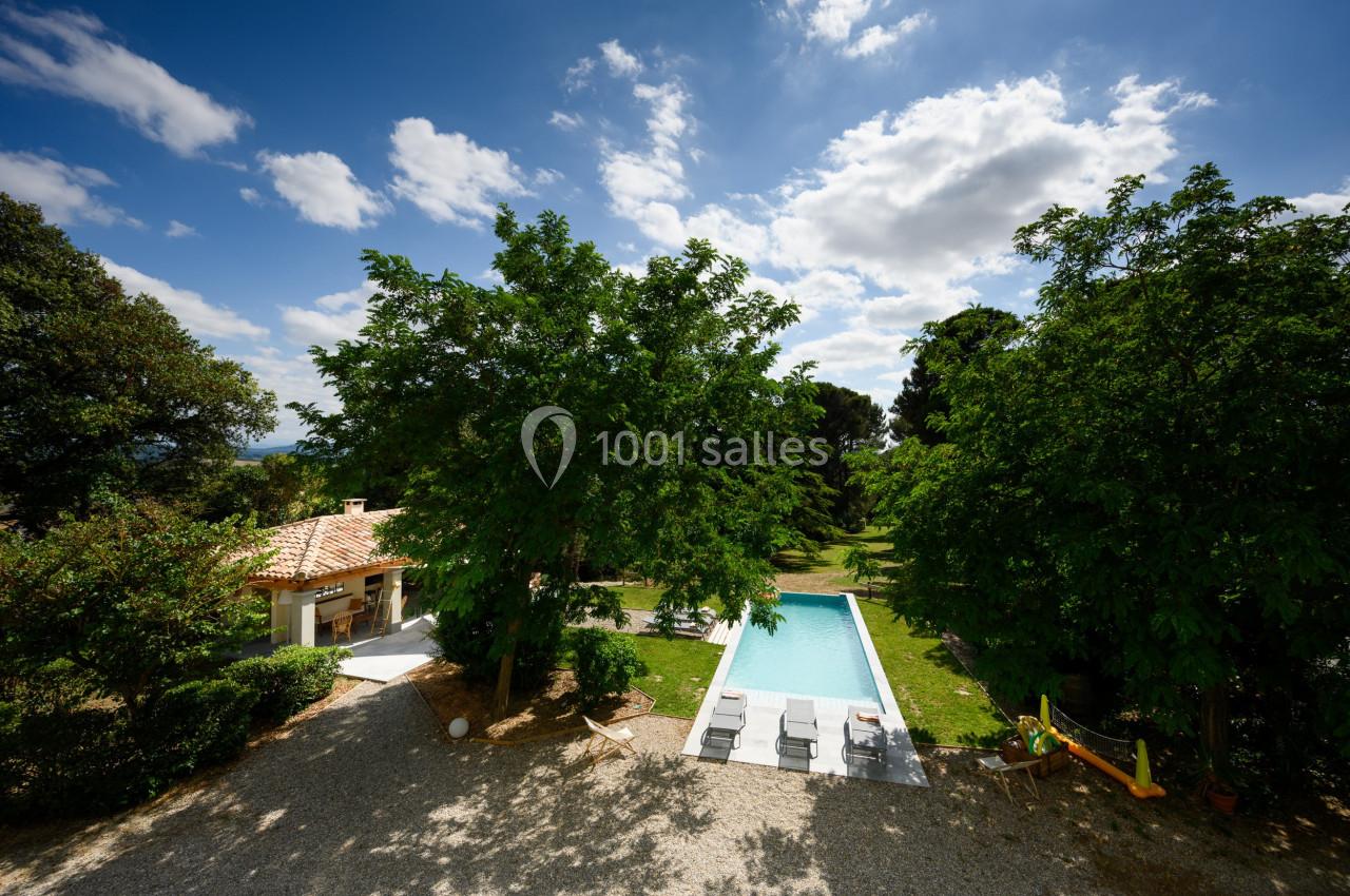 Vue aérienne d'un jardin avec piscine rectangulaire entourée d'arbres, transats et petite maison en arrière-plan.
