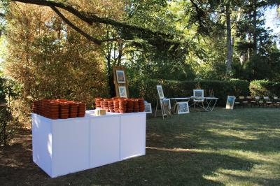 Salle en pierre avec de grandes tables dressées, éclairée par des lustres faits de bouteilles en verre vert.