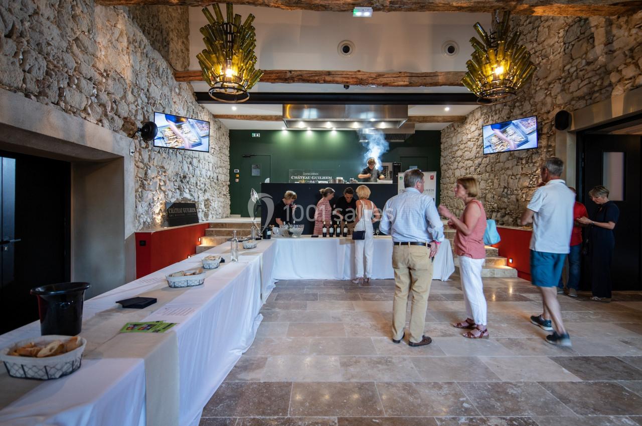 Des personnes dégustent du vin dans une salle en pierre avec un comptoir en arrière-plan et des tables dressées.