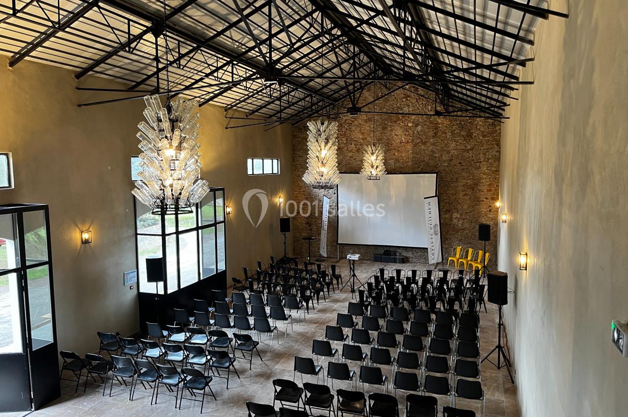 Salle de conférence avec chaises noires alignées, écran de projection, projecteurs et murs en briques apparentes.