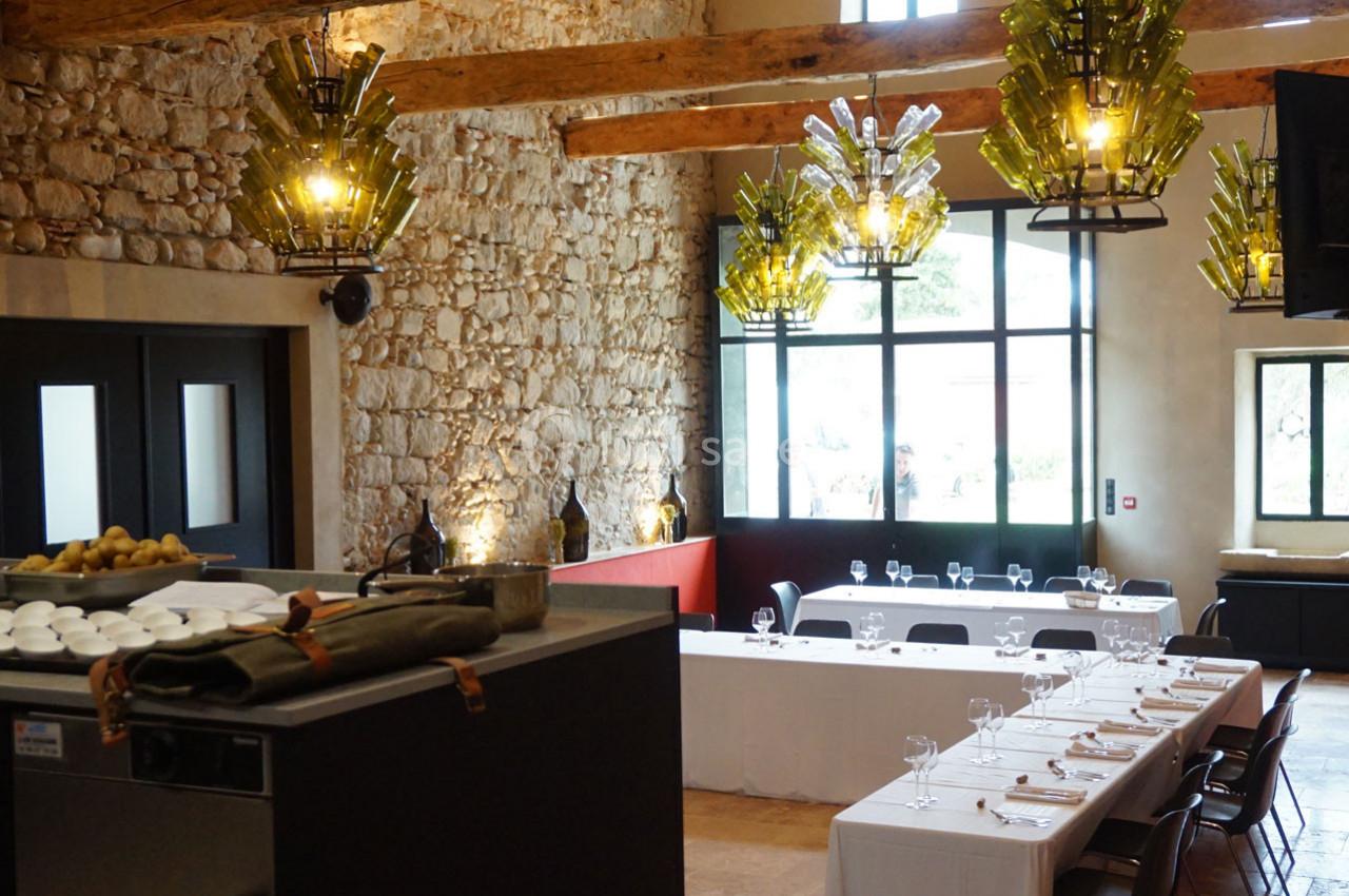 Salle de réception lumineuse avec murs en pierre, poutres apparentes, tables dressées et lustres modernes en verre.