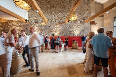Salle en pierre avec de grandes tables dressées, éclairée par des lustres faits de bouteilles en verre vert.