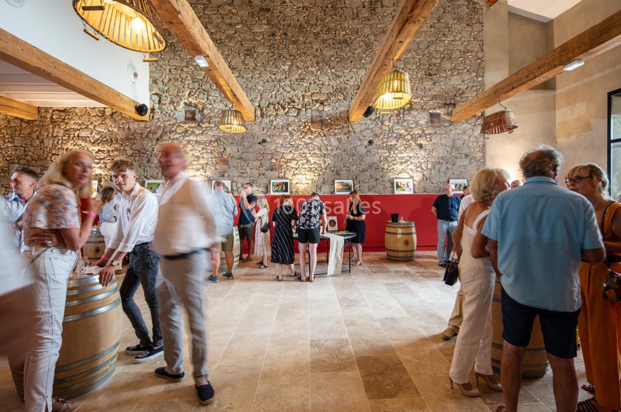 Personnes rassemblées dans une salle lumineuse avec murs en pierre, poutres apparentes et expositions murales.