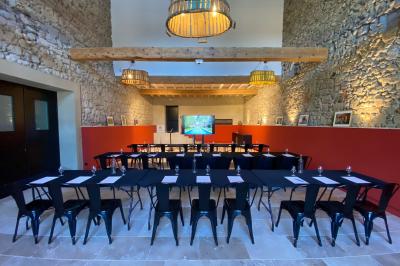 Salle en pierre avec de grandes tables dressées, éclairée par des lustres faits de bouteilles en verre vert.