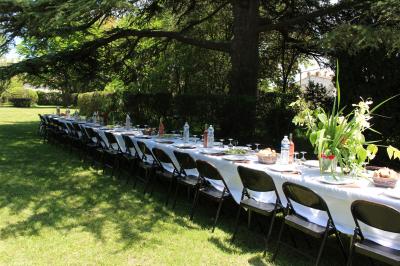 Salle en pierre avec de grandes tables dressées, éclairée par des lustres faits de bouteilles en verre vert.