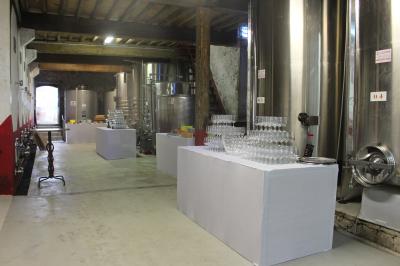 Salle en pierre avec de grandes tables dressées, éclairée par des lustres faits de bouteilles en verre vert.